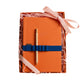 Orange notebook with a pen and ribbon in a decorative box on a white background